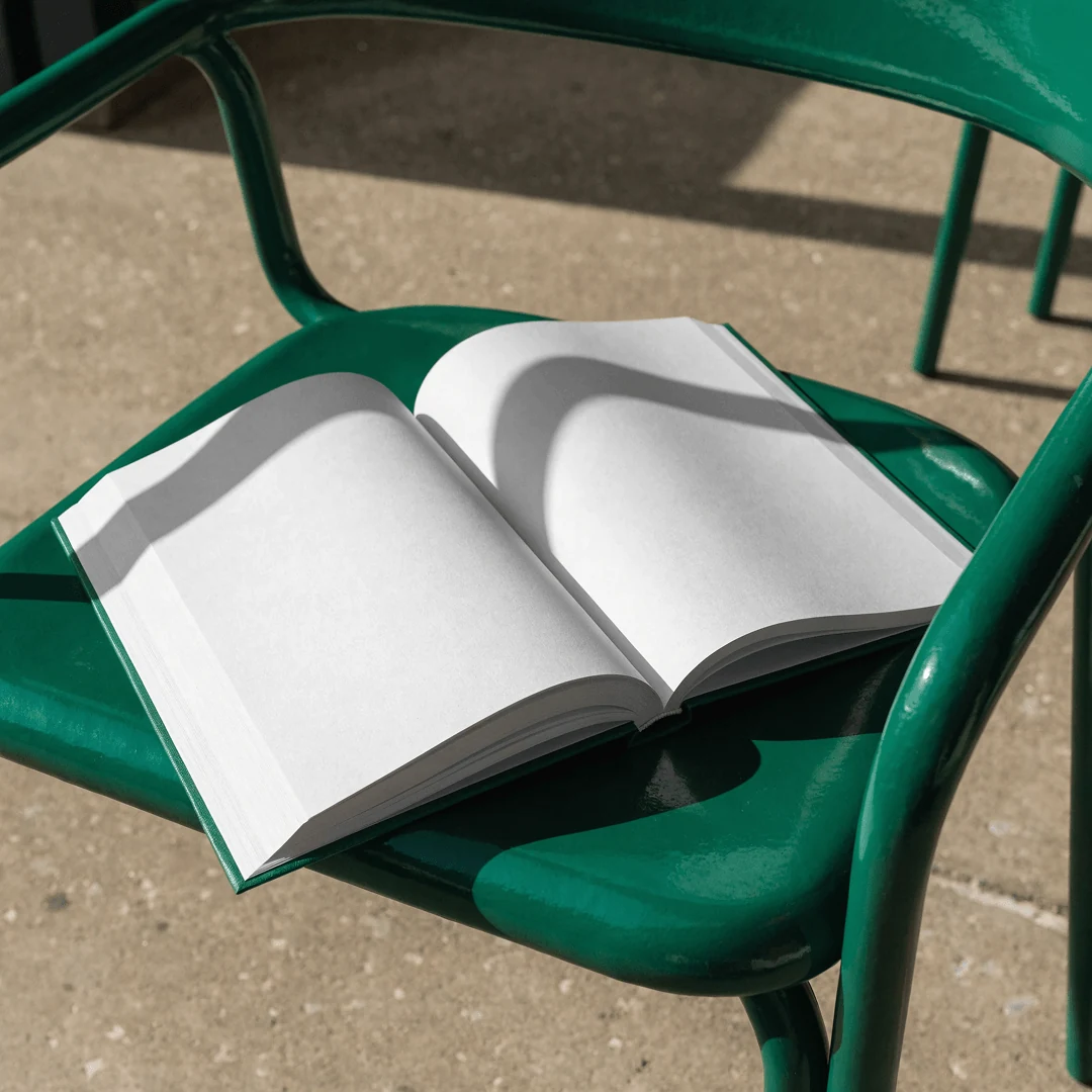 Открытая книга с чистыми страницами на зелёном стуле в солнечном свете